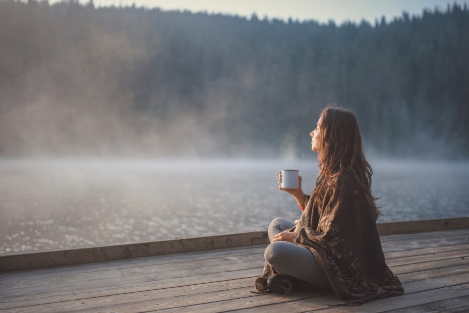 Donna seduta davanti al lago con una tazza in mano